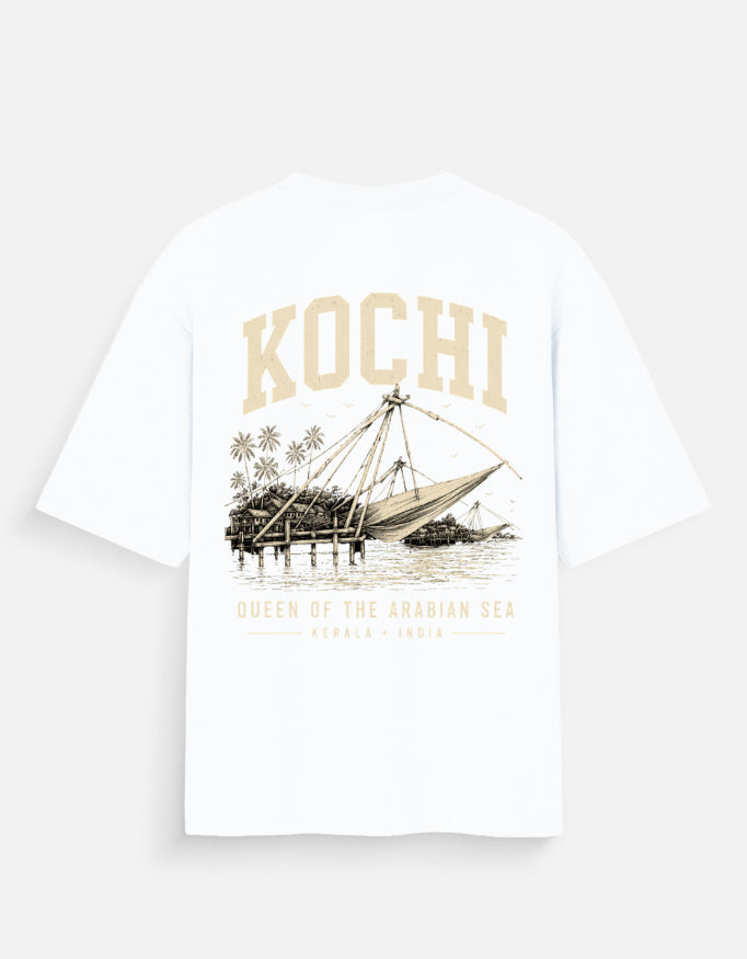 A white short-sleeve t-shirt with a vintage-style graphic on the back featuring the word 'KOCHI' in beige, an illustration of a traditional fishing boat, and text reading 'QUEEN OF THE ARABIAN SEA' and 'KERALA - INDIA'.
