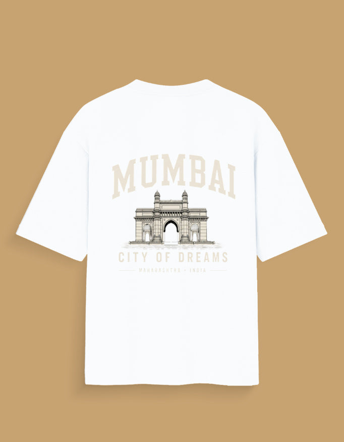 A white short-sleeve t-shirt with a graphic print of the Mumbai Gateway on the back and the text 'MUMBAI CITY OF DREAMS' in beige, displayed against a solid tan background.