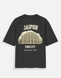 A black short-sleeve t-shirt with a cream-colored graphic print on the back. The graphic features an illustration of the Jaipur Pink City building, with the text 'JAIPUR', 'PINK CITY', and 'RAJASTHAN - INDIA' printed around it.