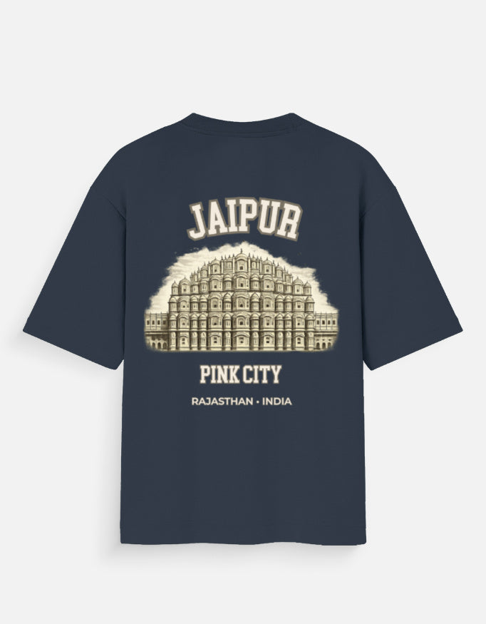 A navy blue short-sleeve t-shirt with a cream-colored graphic print on the back. The graphic features an illustration of the Jaipur Pink City (Rajmandar Palace) with the text 'JAIPUR', 'PINK CITY', and 'RAJASTHAN - INDIA' printed around it.