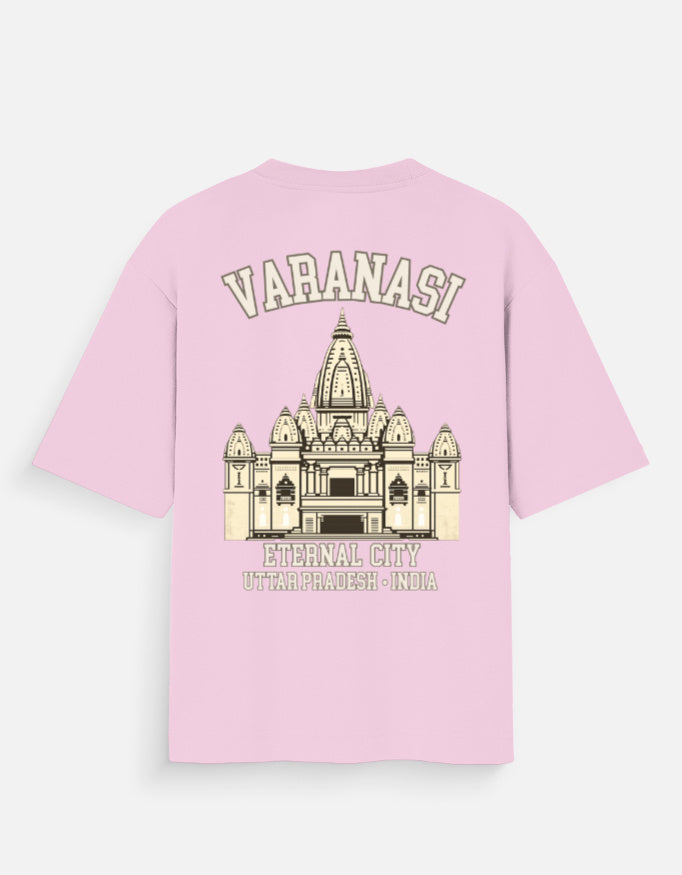 A light pink short-sleeve t-shirt with a graphic print of the Varanasi Eternal City temple on the front, featuring the text 'VARANASI' and 'ETERNAL CITY UTTarPRADESH - INDIA' in a cream color.