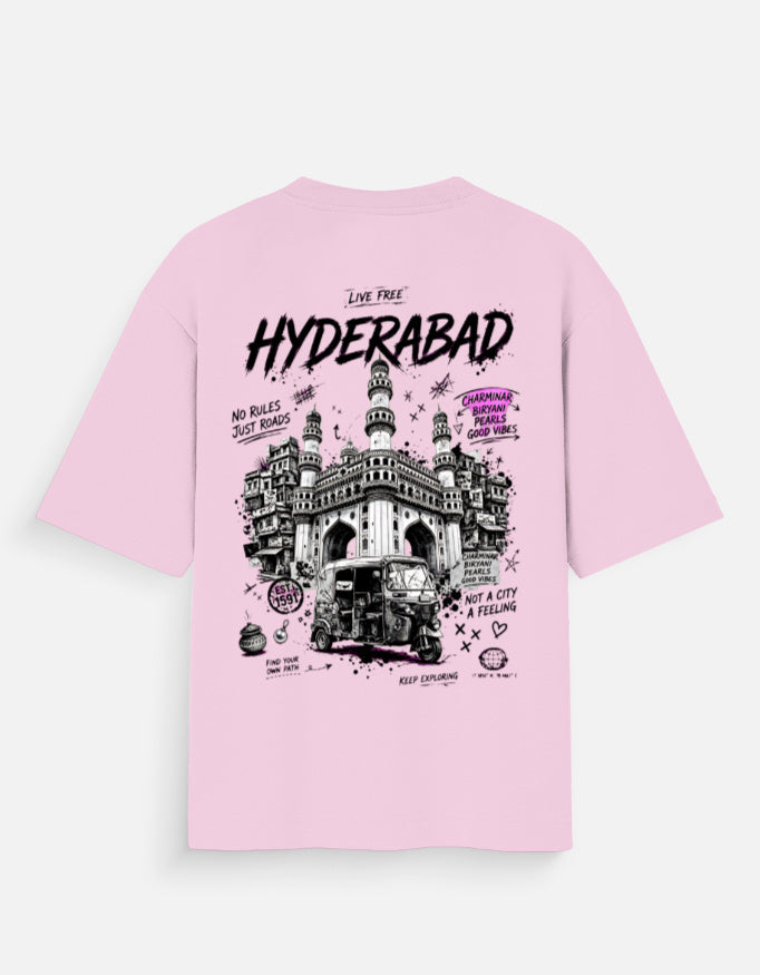 A light pink short-sleeve t-shirt with a large graphic print on the front depicting the Hyderabad Charminar and a rickshaw, with text including 'LIVE FREE HYDERABAD'.