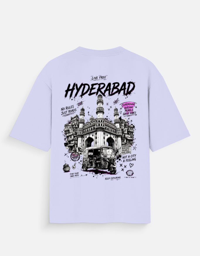 A light lavender short-sleeve t-shirt shown from the back, featuring a large graphic print of the Charminar in Hyderabad with black and purple text and illustrations.