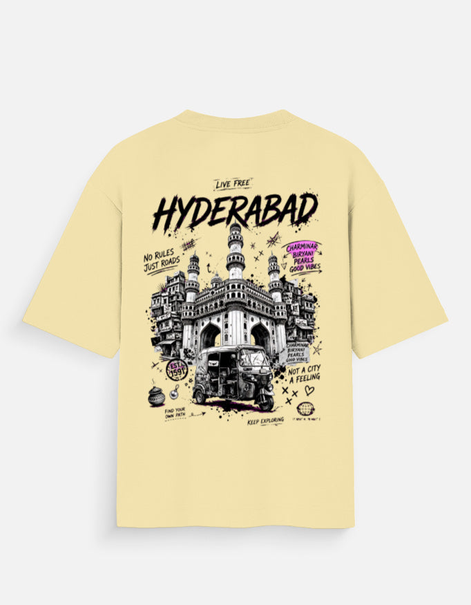A pale yellow t-shirt shown from the back, featuring a large graphic print of the Hyderabad Charminar and a rickshaw with black, white, and purple text details.