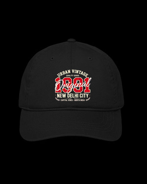 A black baseball cap featuring a red and white graphic print on the front that reads 'URBAN VINTAGE Original 1981 NEW DELHI CITY'. The cap is photographed against a solid black background.