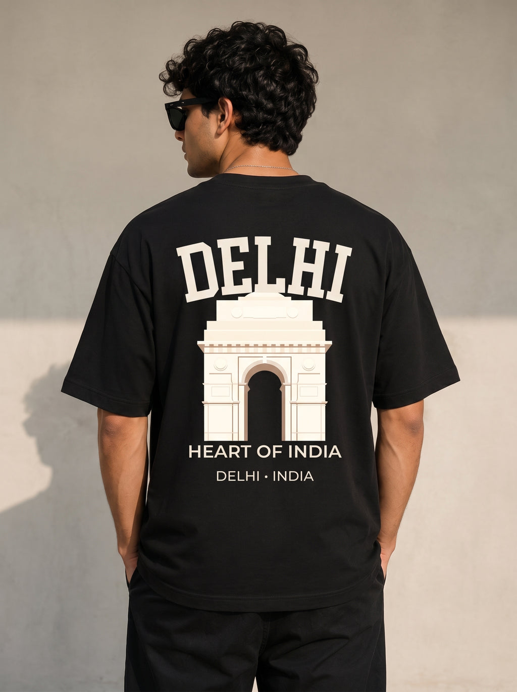 A man viewed from behind wearing a black t-shirt with a large white graphic print of the Delhi Arch and the text 'DELHI HEART OF INDIA'.