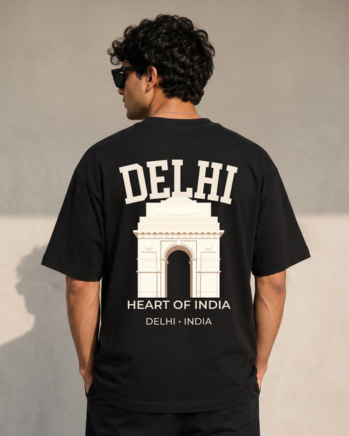 A man viewed from behind wearing a black t-shirt with a large white graphic print of the Delhi Arch and the text 'DELHI HEART OF INDIA'.
