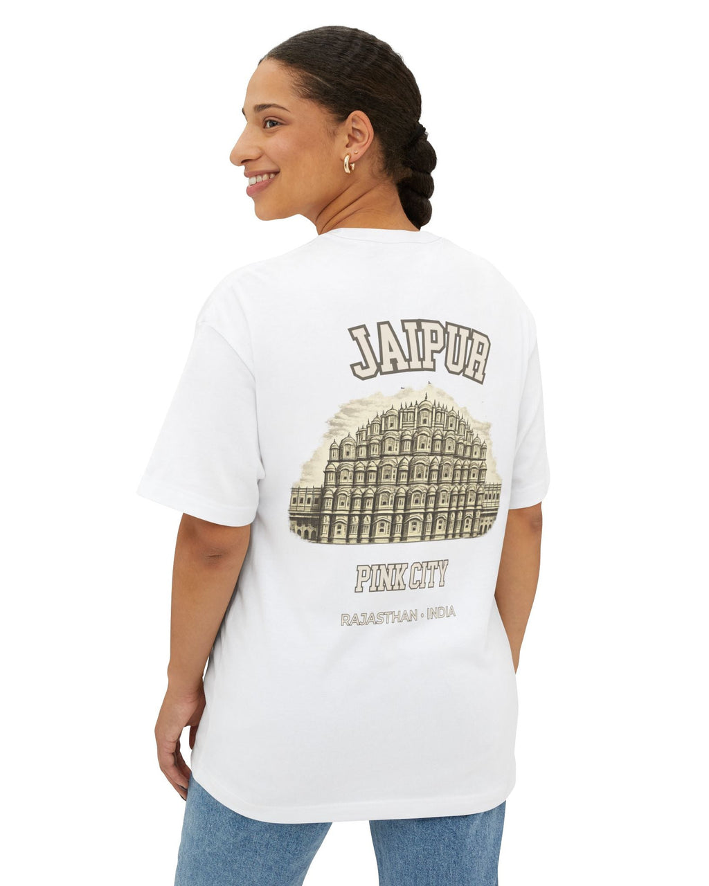 A woman shown from the back wearing a white graphic T-shirt with 'JAIPUR' and a large palace illustration printed on the back, paired with blue jeans against a plain white studio background.