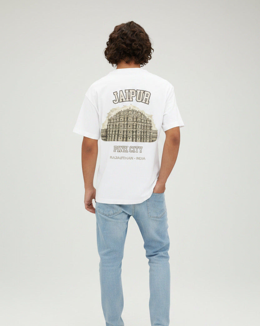 A man viewed from behind wearing a white t-shirt with a large graphic print of the Jaipur Pink City palace on the back, paired with light blue jeans, against a plain white background.