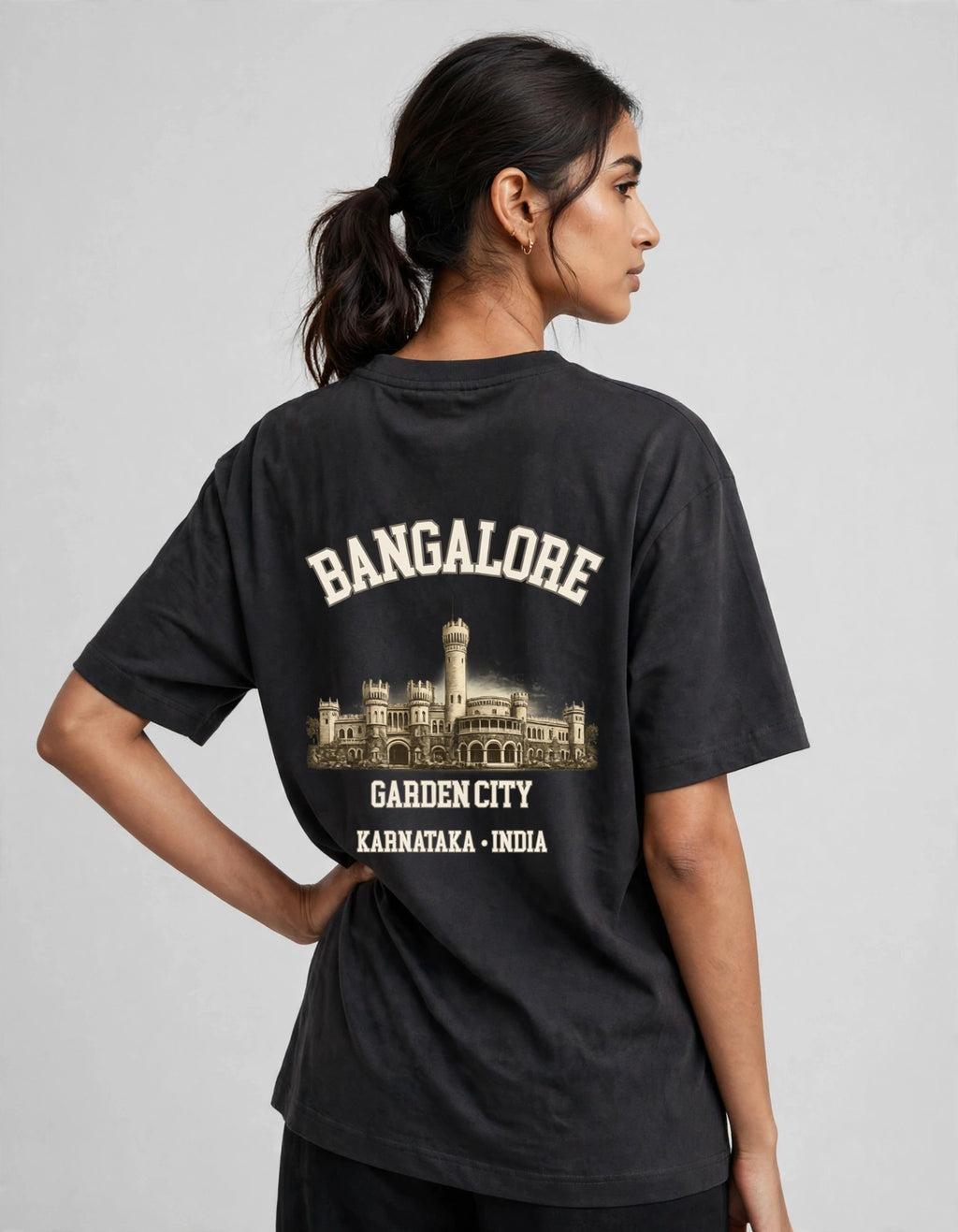 A woman shown from the back wearing a faded black graphic t-shirt with cream-colored text reading 'BANGALORE' and 'GARDEN CITY KARNATAKA - INDIA' above and below a building illustration.