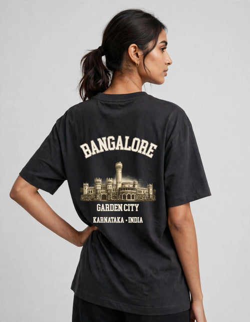 A woman shown from the back wearing a faded black graphic t-shirt with cream-colored text reading 'BANGALORE' and 'GARDEN CITY KARNATAKA - INDIA' above and below a building illustration.