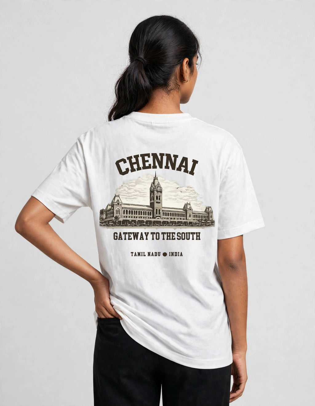 A woman shown from the back wearing a white t-shirt with a dark brown graphic print of the Chennai Municipal Council building and the text 'CHENNAI GATEWAY TO THE SOUTH'.
