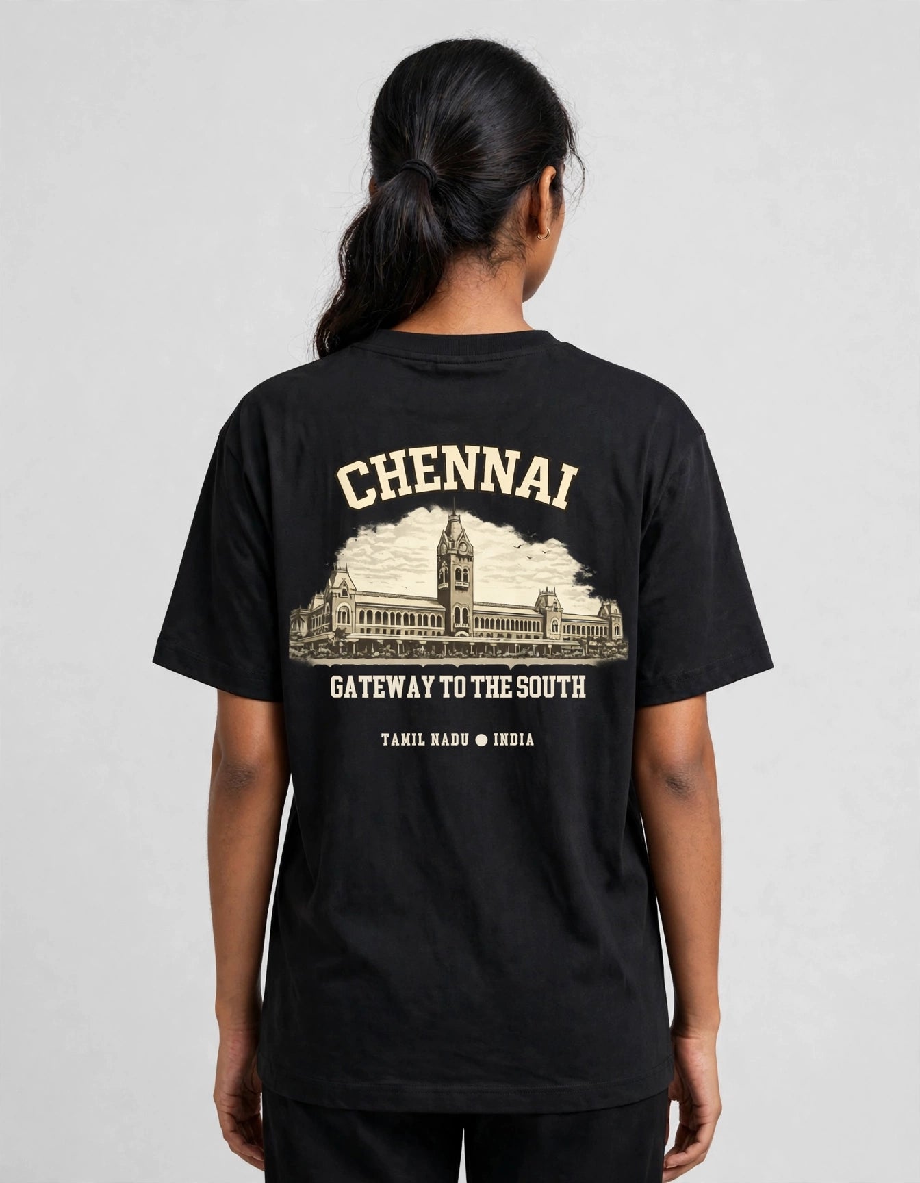 A woman viewed from the back wearing a black short-sleeve T-shirt with a large cream-colored graphic print on the back. The print features the word 'CHENNAI' above an illustration of a historic building, with the text 'GATEWAY TO THE SOUTH' and 'TAMIL NADU • INDIA' below.