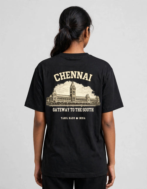 A woman viewed from the back wearing a black short-sleeve T-shirt with a large cream-colored graphic print on the back. The print features the word 'CHENNAI' above an illustration of a historic building, with the text 'GATEWAY TO THE SOUTH' and 'TAMIL NADU • INDIA' below.