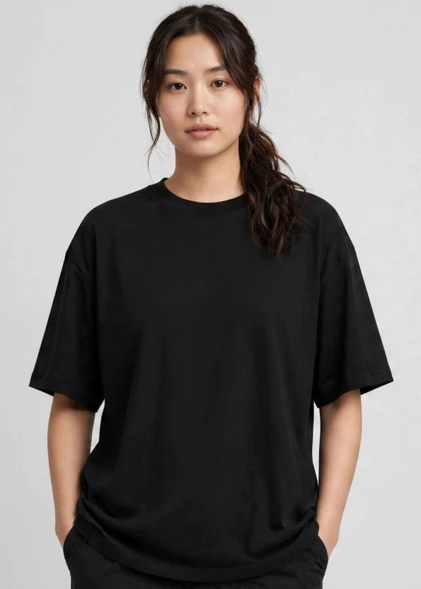 A woman modeling a black short-sleeve crewneck t-shirt with a small gold chest graphic, paired with black cargo pants, against a light gray studio background.