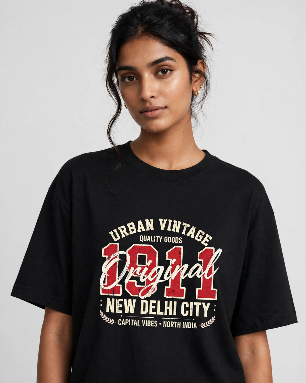 A woman wearing a black oversized graphic t-shirt with a vintage-style cream and red print reading 'Urban Vintage Original New Delhi City 1911'.