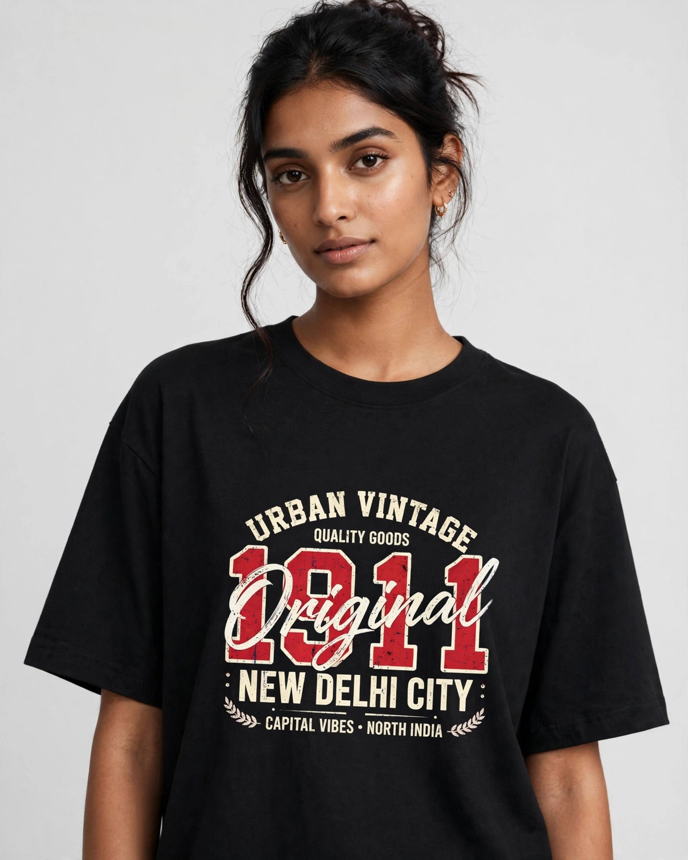A woman wearing a black oversized graphic t-shirt with a vintage-style cream and red print reading 'Urban Vintage Original New Delhi City 1911'.