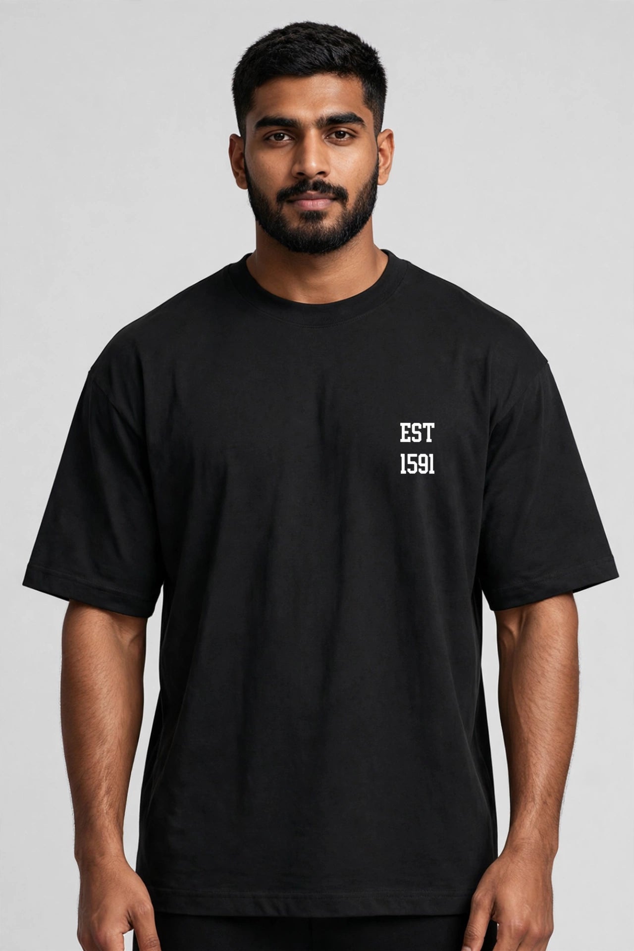 A man wearing a black short-sleeve t-shirt with 'EST 1591' printed in white on the left chest, photographed against a neutral gray background.
