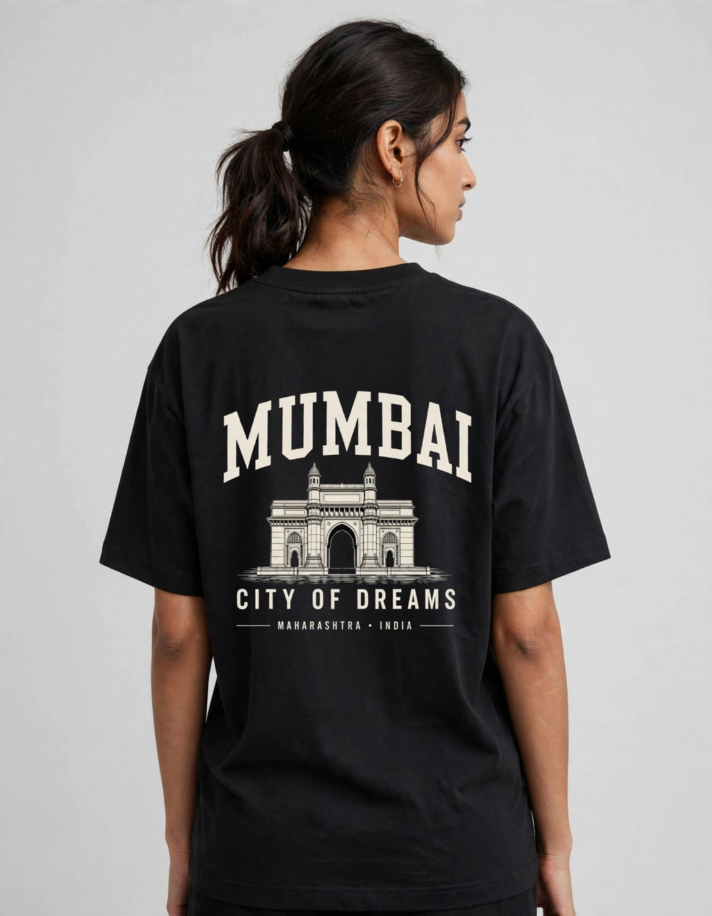 A woman shown from the back wearing a black t-shirt with a large cream-colored graphic print of Mumbai's Gateway of India and the text 'MUMBAI CITY OF DREAMS'.