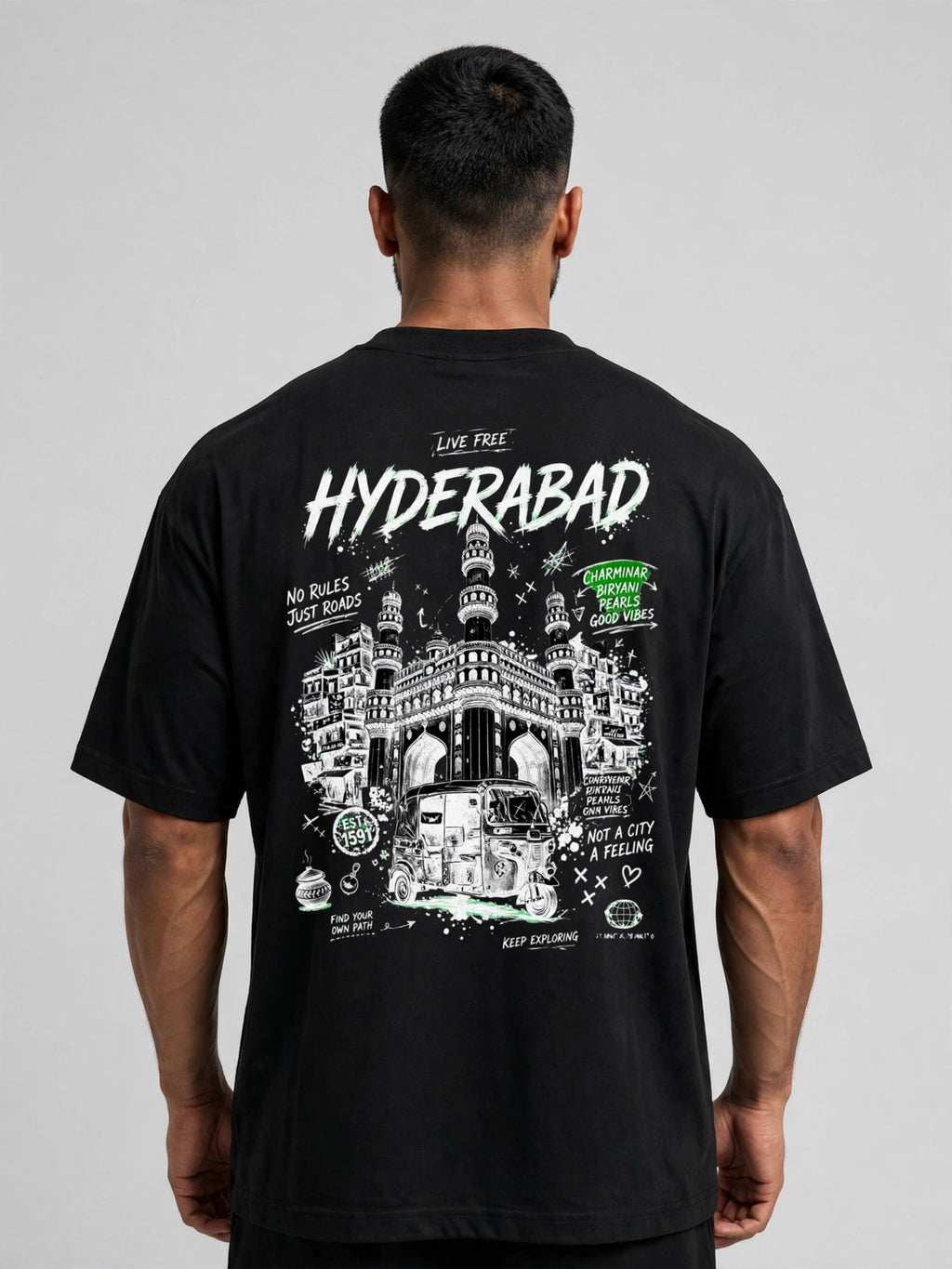 A man viewed from the back wearing a black t-shirt with a large white and green graphic print of the Hyderabad Charminar and a van, featuring the text 'HYDERABAD' and 'LIVE FREE!'.