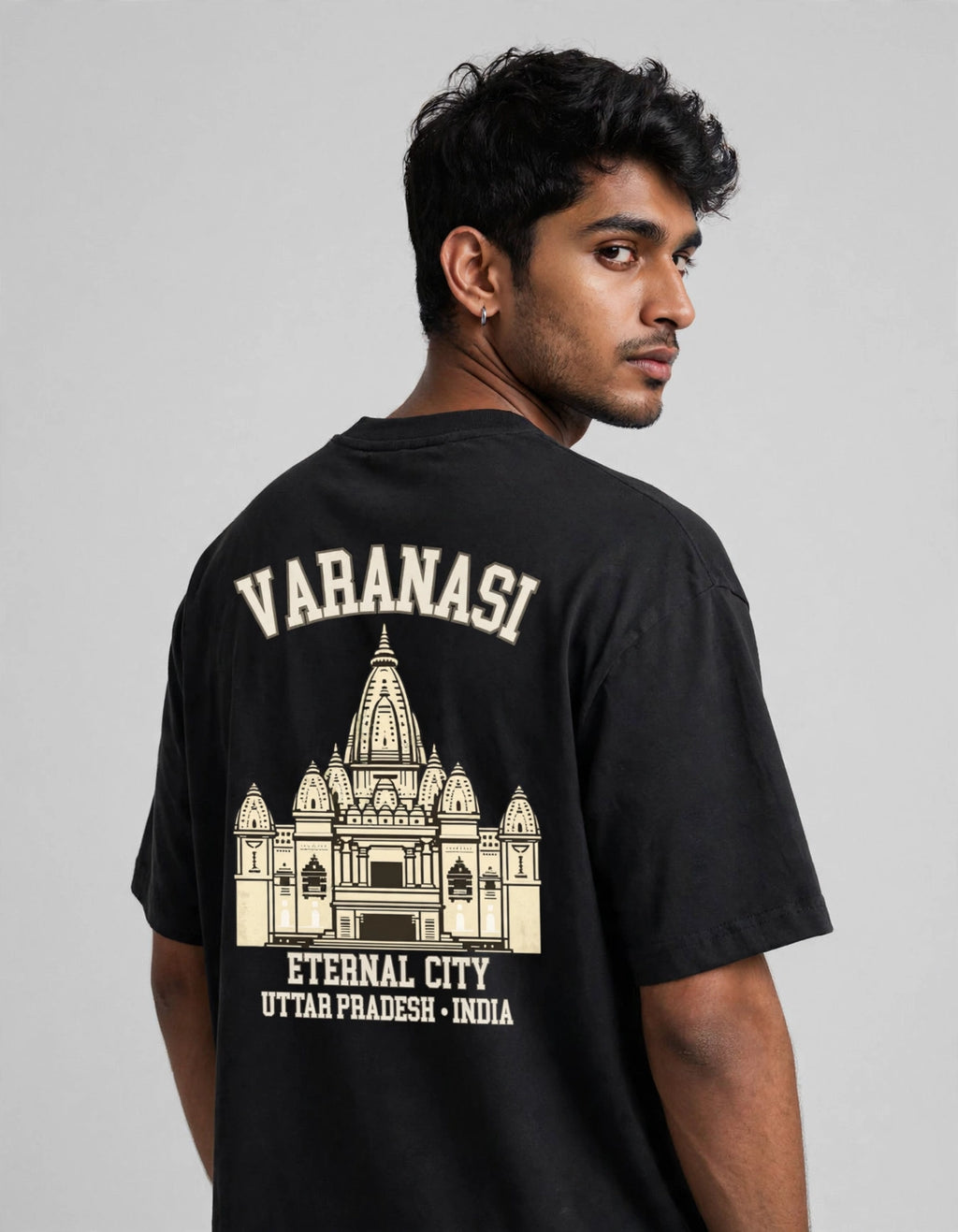 A man wearing a black t-shirt, viewed from the back. The shirt features a cream-colored graphic print of the Varanasi temple with the text 'VARANASI' and 'ETERNAL CITY UTTAR PRADESH - INDIA'.