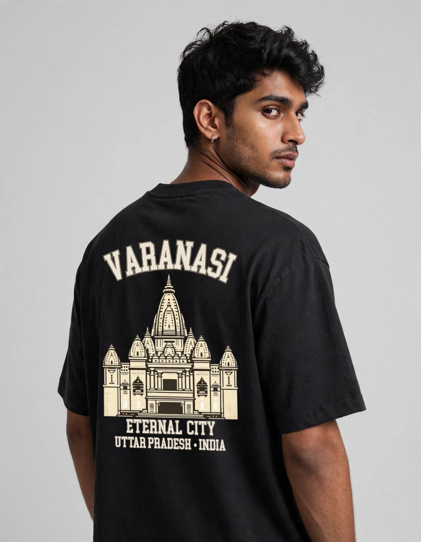 A man wearing a black t-shirt, viewed from the back. The shirt features a cream-colored graphic print of the Varanasi temple with the text 'VARANASI' and 'ETERNAL CITY UTTAR PRADESH - INDIA'.