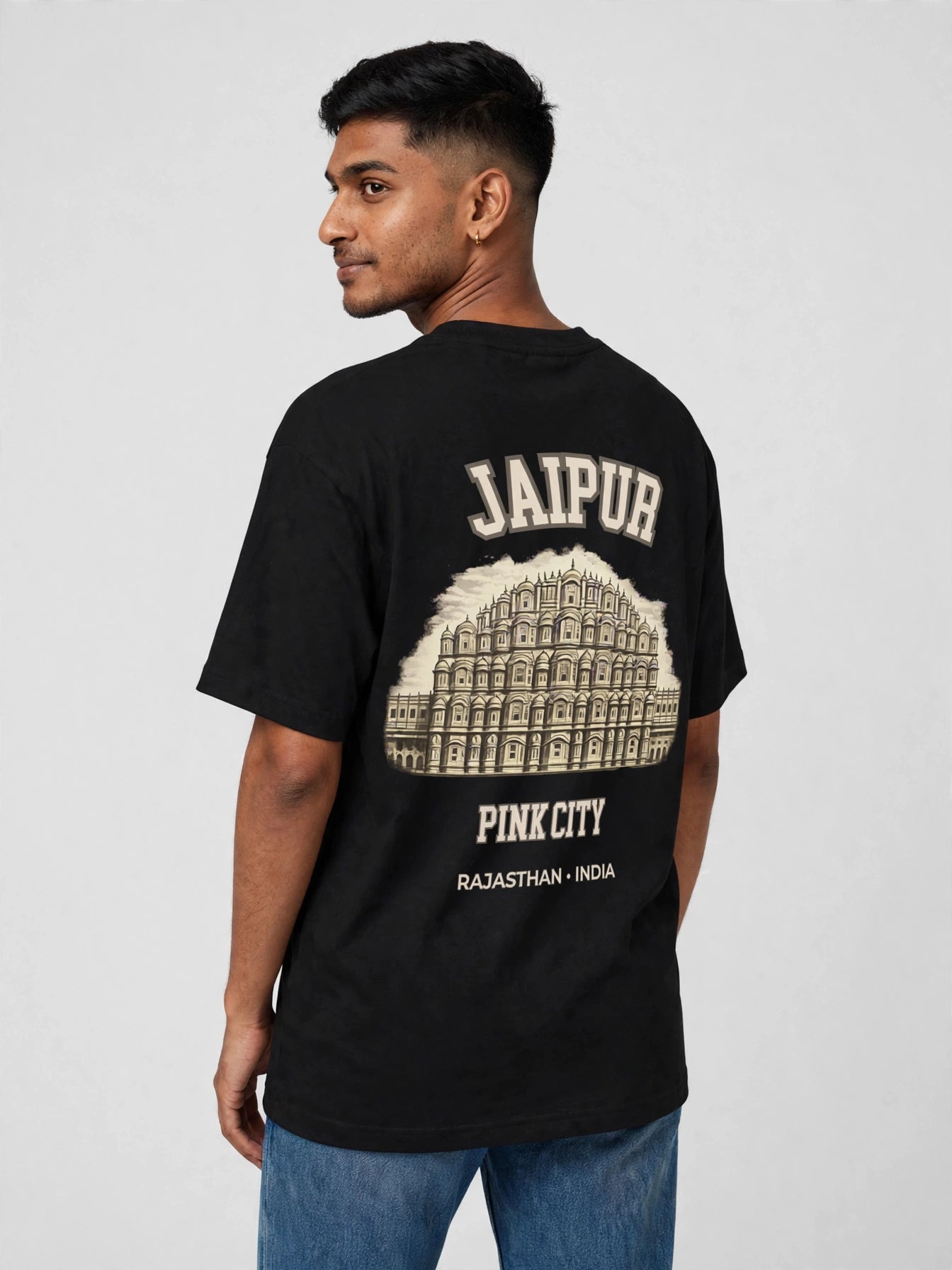 A man wearing a black t-shirt with a cream-colored graphic print of Jaipur's Pink City and Arjun Arch, shown from the back against a light gray background.