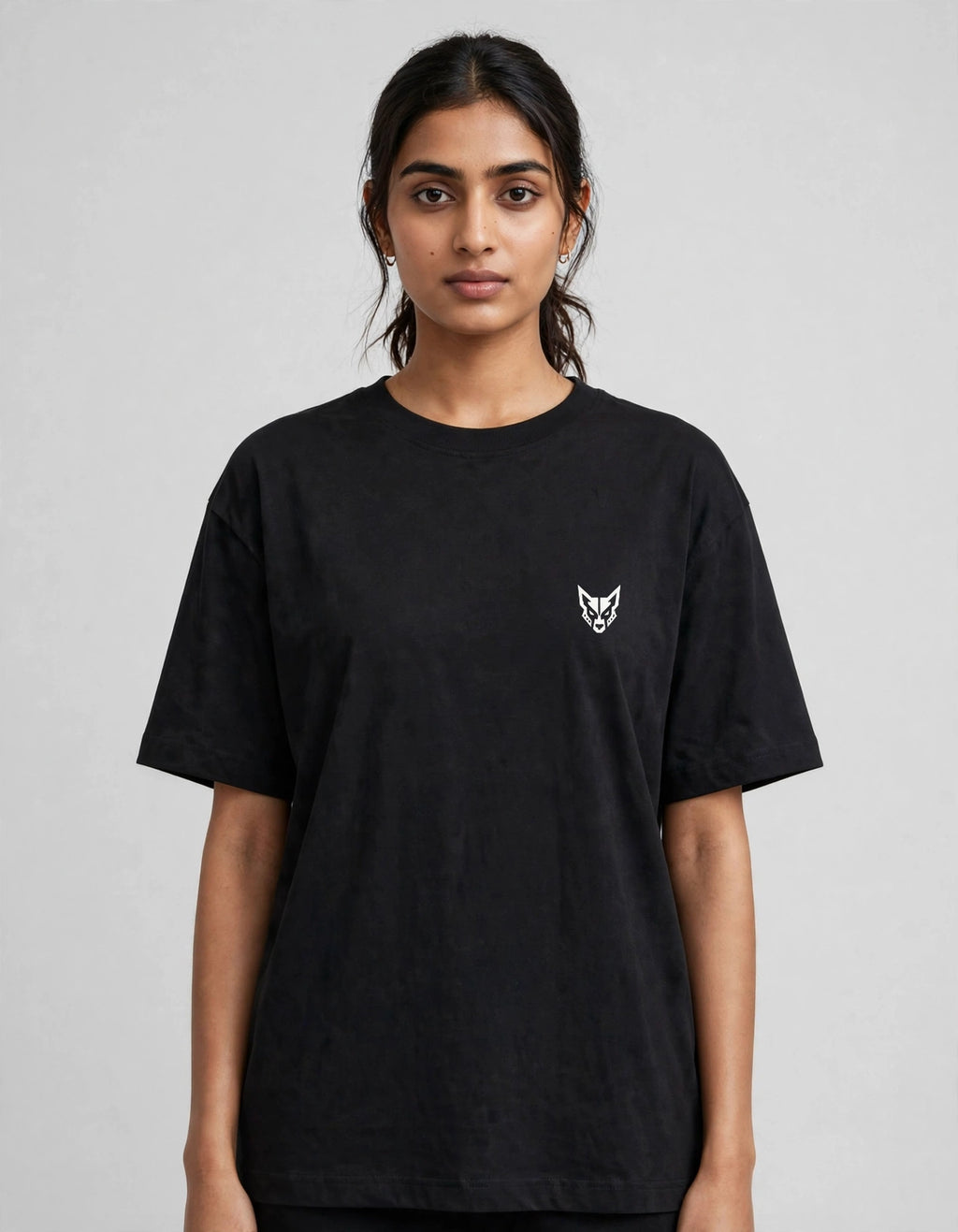 A woman wearing a black short-sleeve crewneck t-shirt with a small white embroidered fox head logo on the left chest, photographed against a neutral gray studio background.